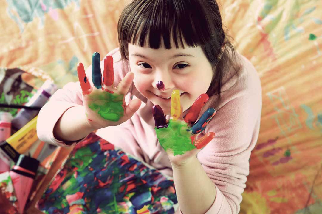 Criança com síndrome de down brincando de colorir com as mãos sujas de tinta