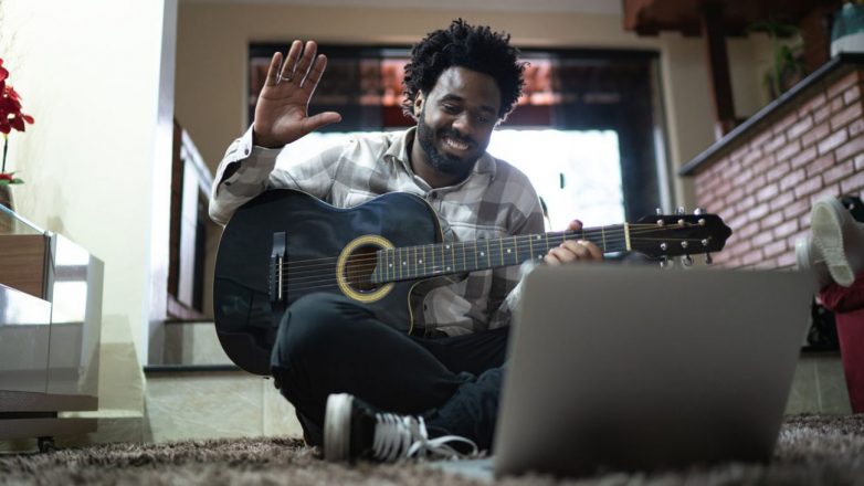 ganhar dinheiro sem sair de casa: Ensinando violão por meio de uma videochamada, acenando para um laptop