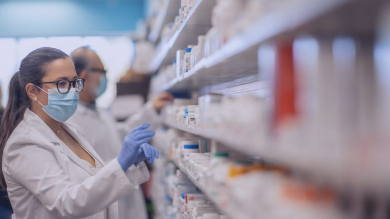 Farmacêutico que trabalha em uma farmácia organizando produtos enquanto usa máscara protetora durante o surto de coronavírus.