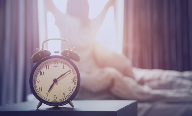 Fugir da rotina: Closeup despertador tendo um bom dia com fundo mulher feliz alongamento na cama depois de acordar, luz do sol da manhã.