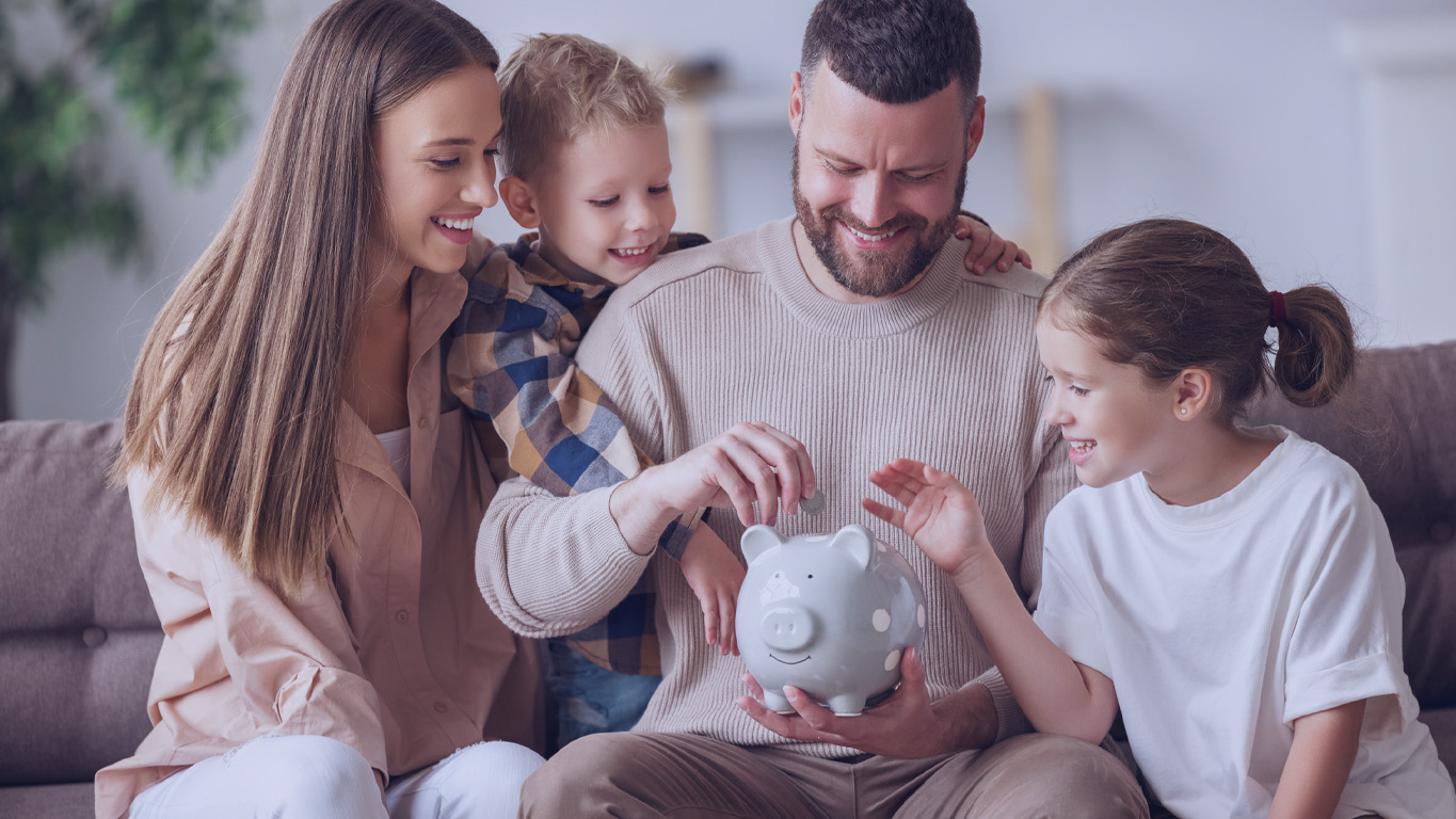 Família feliz: alegre mãe e pai com crianças sorrindo e colocando moedas no cofrinho enquanto está sentado no sofá em casa