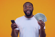 Homem afro-americano animado segurando smartphone e dólares