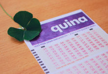 Bilhete da Loteria Quina em cima de mesa de madeira com trevo de quatro folhas ao lado.