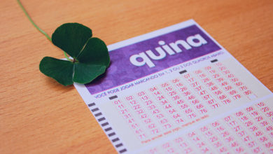 Bilhete da Loteria Quina em cima de mesa de madeira com trevo de quatro folhas ao lado.