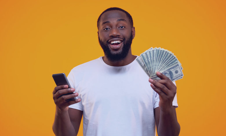 Homem afro-americano animado segurando smartphone e dólares