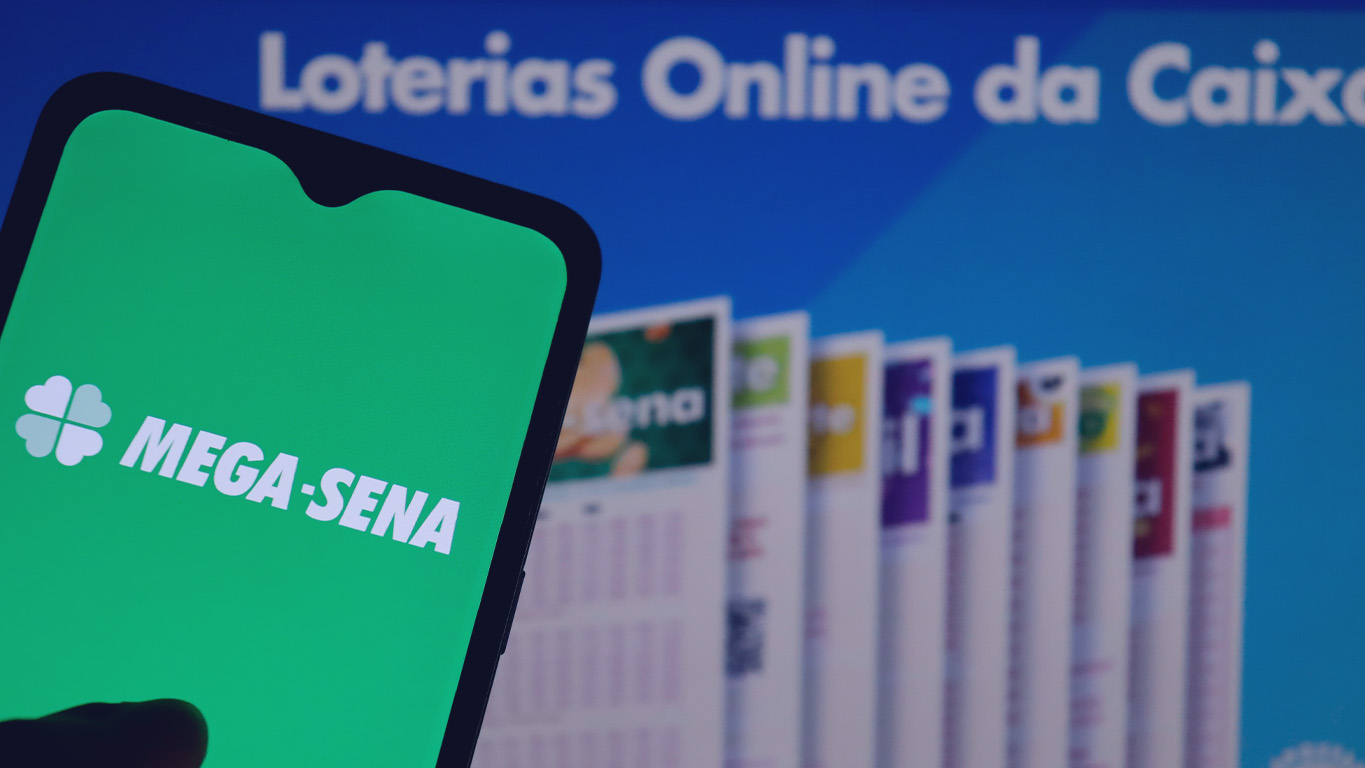 Logo da loteria Mega-Sena na tela do smartphone. E no fundo a escrita Loterias Online Caixa.