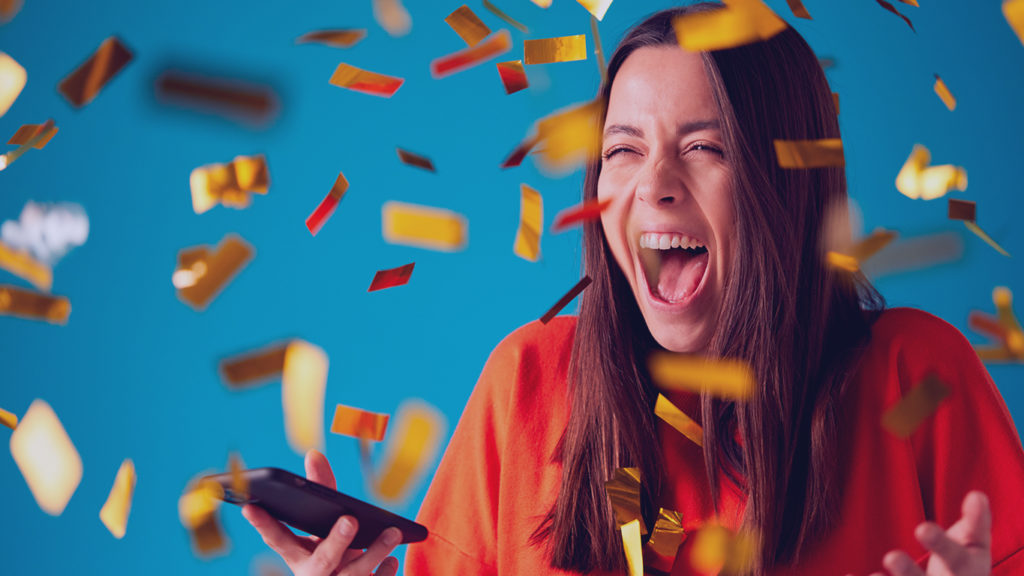 jovem mulher comemorando com um celular na mão e confetes dourados
