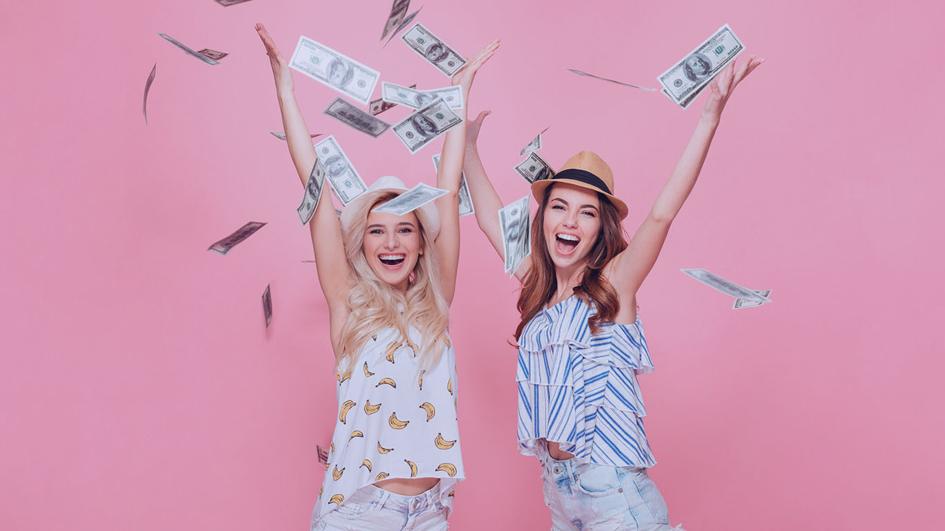 Duas mulheres jogando notas de dinheiro no ar enquanto sorriem.